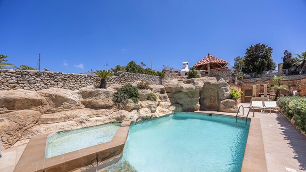 A swimming pool with a stone wall and a small pavilion.