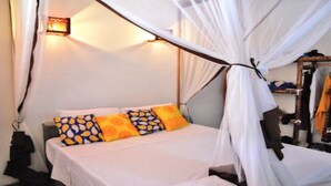 A bed with a canopy, pillows with a leaf pattern, and a wall-mounted light fixture. - Nyumbani Residence- Apartment 3 (Jambiani snc Jambiani)
