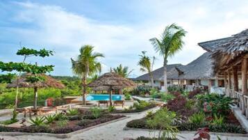 Un complexe hôtelier doté de bâtiments aux toits de chaume, d’une piscine et d’un aménagement paysager de style tropical.
