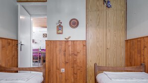 A bedroom with two wooden beds, a wooden wardrobe, a wall clock, and a small decorative plate.