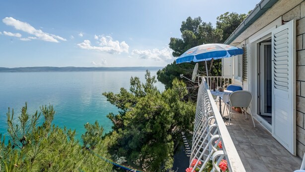 A balcony with a view of a lake, a table with chairs, and a blue umbrella.