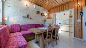A cozy kitchen with a wooden ceiling, a dining table with chairs, a pink patterned sofa, and a white brick wall.