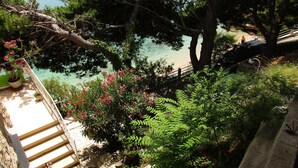 A staircase leading to a balcony overlooking a beach with clear water, surrounded by lush greenery and potted plants.