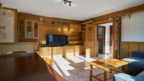 Eine moderne Küche mit Holzschränken, einem integrierten Fernseher und einem Essbereich mit Holztisch und blauem Sofa.