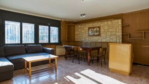 Ein Wohnzimmer mit einer Couch, einem Esstisch mit Stühlen, einer Küchenzeile mit Kühlschrank und einer Steinwand mit Kunstwerken.