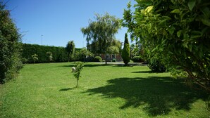 A well-maintained grassy area with a variety of trees and shrubs, a clear sky, and a building in the background. - CASA GAYOL, NEAR THE BEACH OF PORCÍA (El Franco)