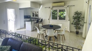 Een moderne keuken met een centraal eiland, een zithoek met een ronde tafel en stoelen, en een balkon met een zwart metalen hekwerk en groene planten.