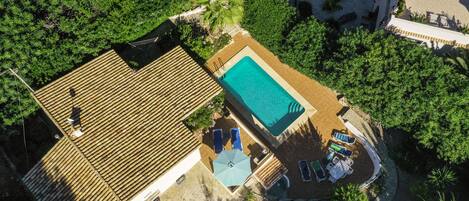 Vista aérea de un resort con piscina, sillones de descanso y una terraza de madera.
