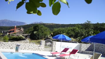 Un espace piscine avec des chaises longues et des parasols, un mur en pierre et une villa appelée « Villa Rogac ».