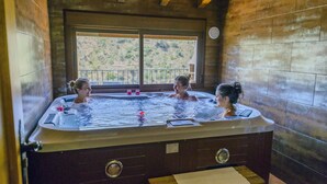 A hot tub with three people in it, wooden walls, and a window with a view of a hilly landscape. - RURAL HOUSE "TENGUERENGUE" (Laroya, Almería)