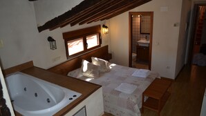 Une chambre à coucher avec une grande baignoire, une tête de lit en bois, une table de chevet et une fenêtre avec des stores.