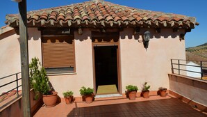 Un bâtiment avec un toit recouvert de tuiles, une porte en bois et un petit balcon agrémenté de plantes en pot.