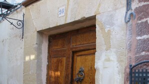Une porte en bois ornée d’un heurtoir en métal, flanquée de deux plantes en pot, qui donne sur un escalier en pierre.