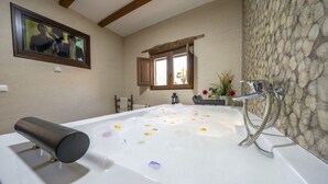 A bathroom with a bathtub filled with water and rose petals, a wooden window, and a stone wall. - Rural house (rental entire) Reul Alto Cortijos Rurales for 2 people (Laroya)