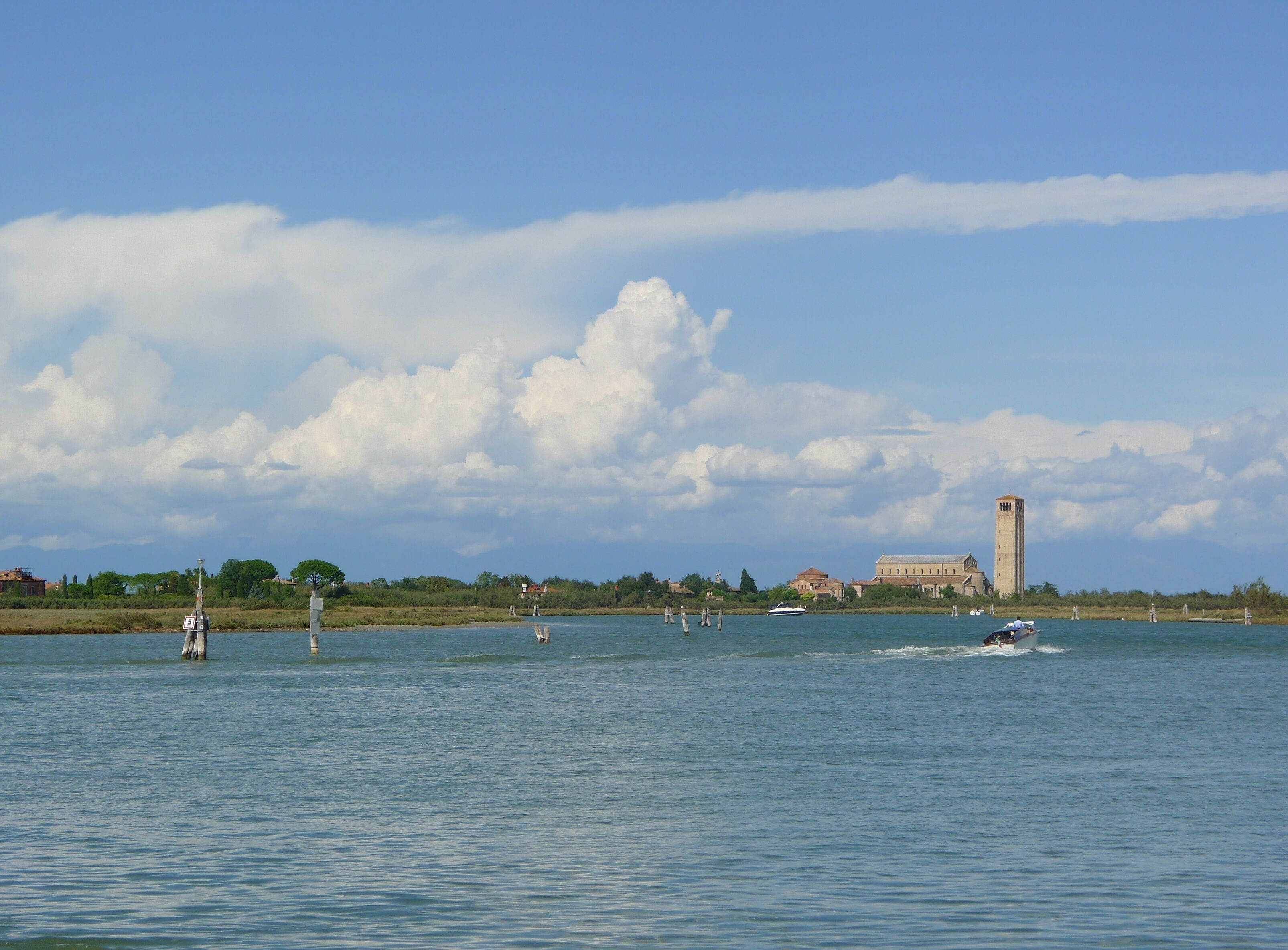 Ein ruhiger See mit Booten, einem Turm und Gebäuden im Hintergrund.