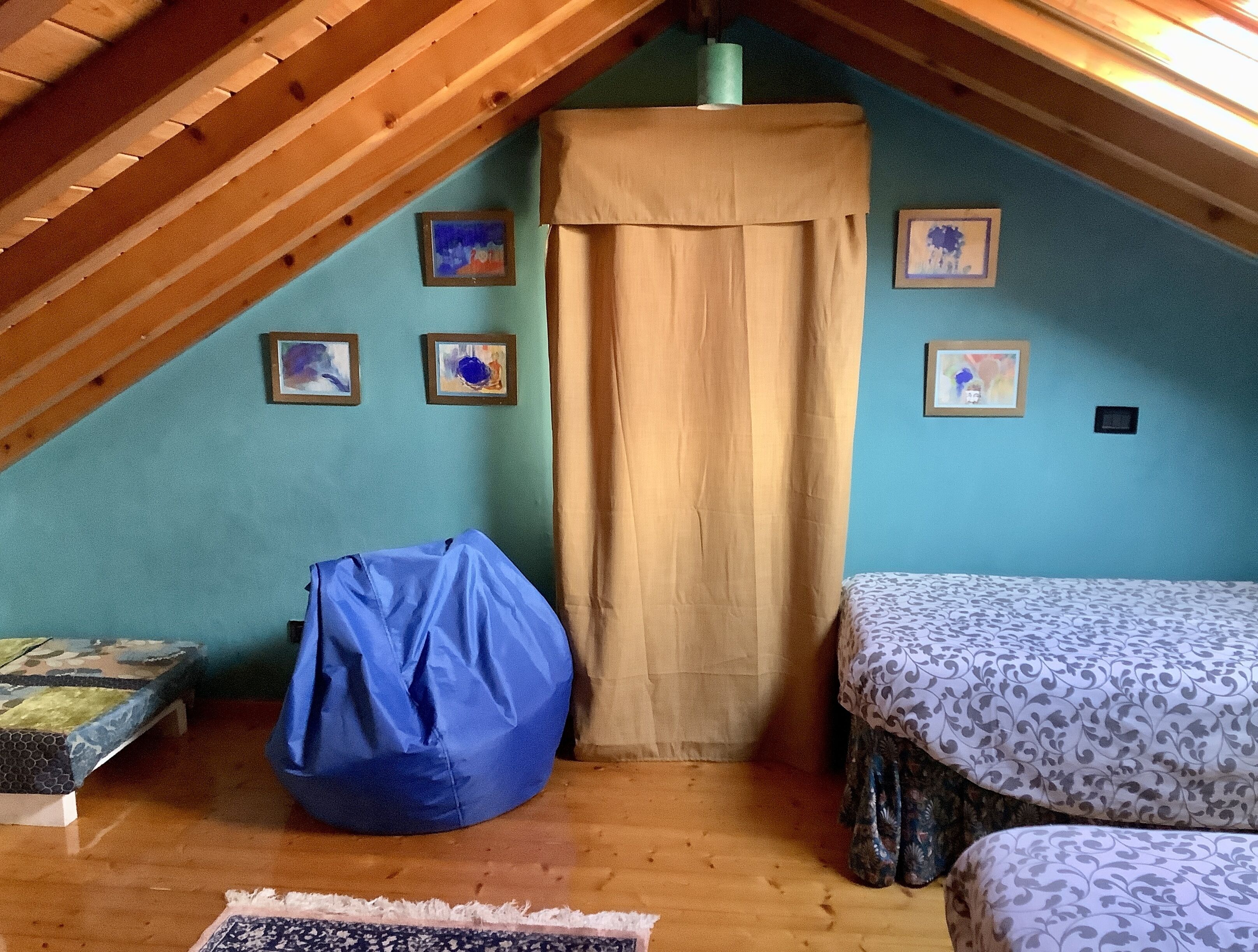 Una piccola camera mansardata con soffitto spiovente, una poltrona sacco blu, due letti con decorazioni e diverse immagini incorniciate alle pareti.