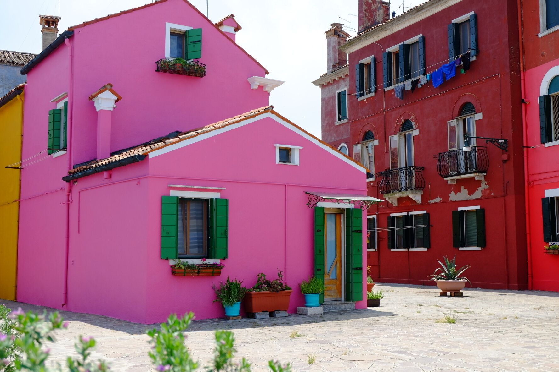 Ein pinkfarbenes Gebäude mit grünen Fensterläden und einer Tür, umgeben von bunten Gebäuden.