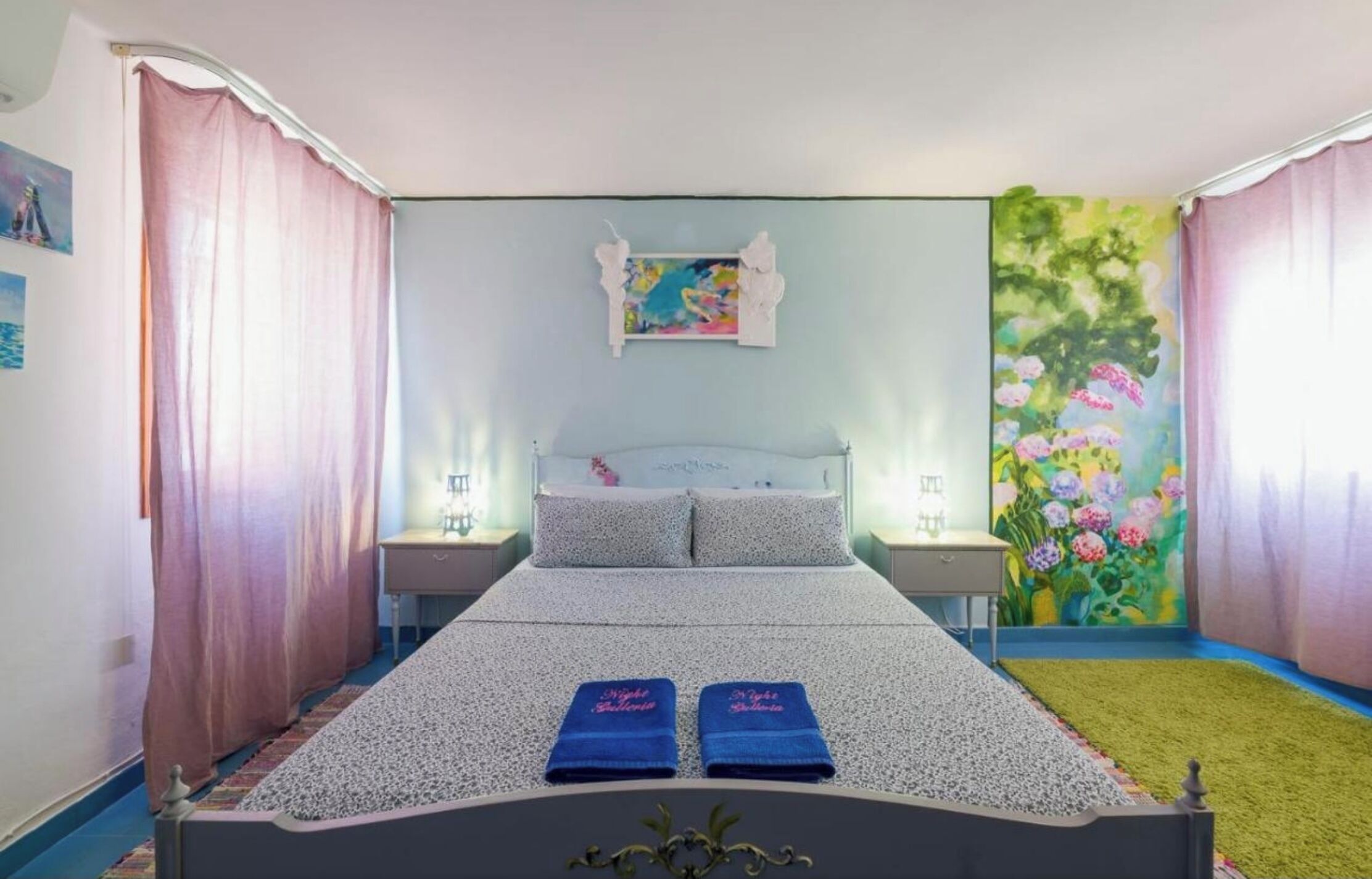 A bedroom with a bed, two nightstands, a painting, and a floral mural.