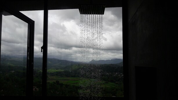 Vista a través de una ventana con lluvia torrencial, una puerta y un paisaje de campos verdes y montañas.