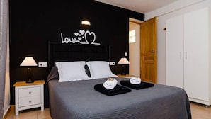 A neatly made bed with a dark grey bedspread, two white pillows, and two towels on a wooden nightstand with a lamp. - Villa los Naranjos Calpe (Calpe)