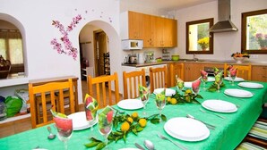 A dining area with a long table set for a meal, wooden chairs, and a kitchen in the background. - Villa los Naranjos Calpe (Calpe)