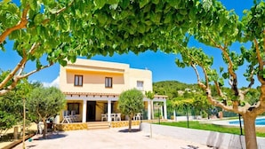 A two-story building with a yellow facade, a covered patio with outdoor seating, and a pool area in the background. - Villa los Naranjos Calpe (Calpe)