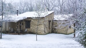 Une maison recouverte de neige, avec un toit en pente, entourée d’arbres sans feuilles et d’un paysage enneigé.