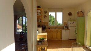 A kitchen with wooden cabinets, a refrigerator, and a window with a view of greenery.