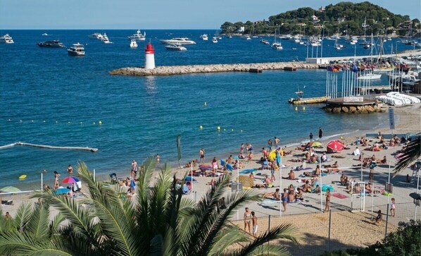 A beach with people sunbathing, a lighthouse, and boats in the water.