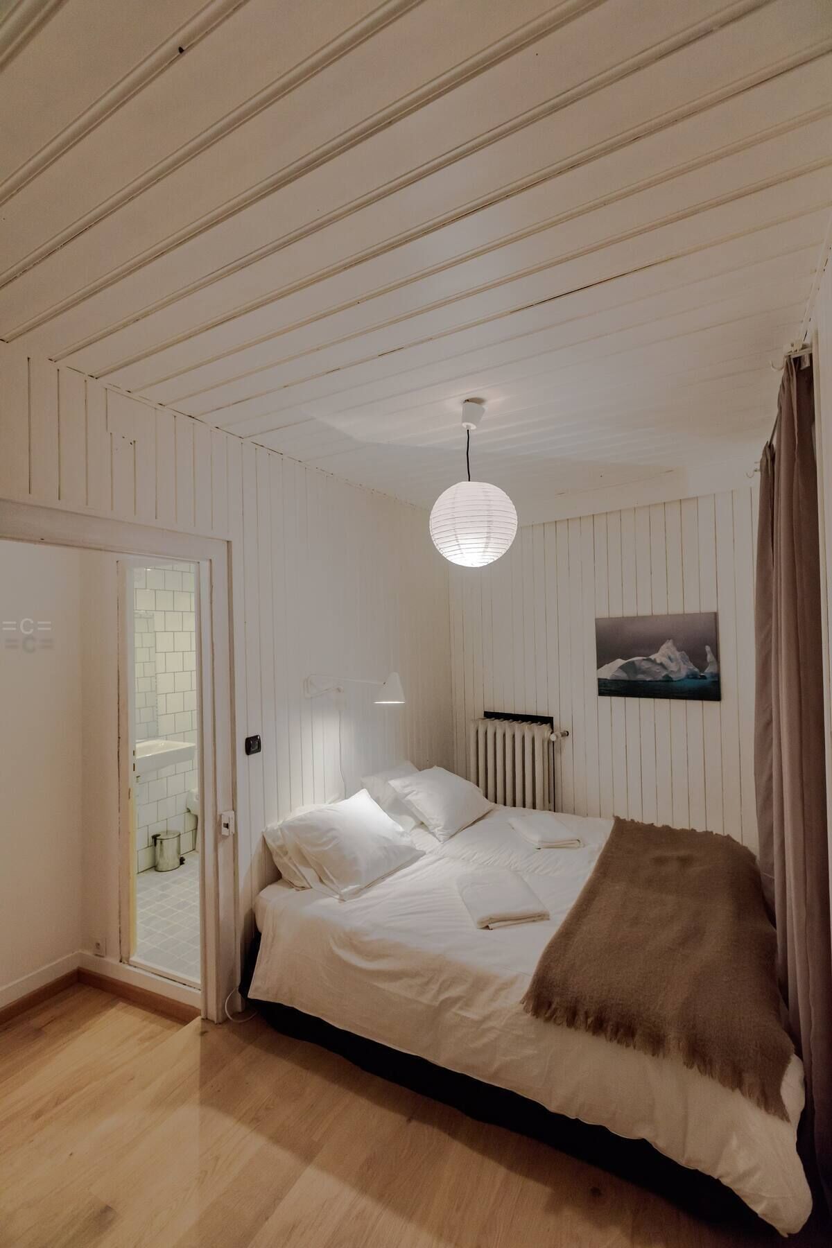 Une pièce avec un lit, un luminaire suspendu, un radiateur et un tableau au mur.