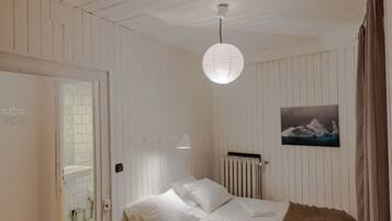 Une pièce avec un lit, un luminaire suspendu, un radiateur et un tableau au mur.