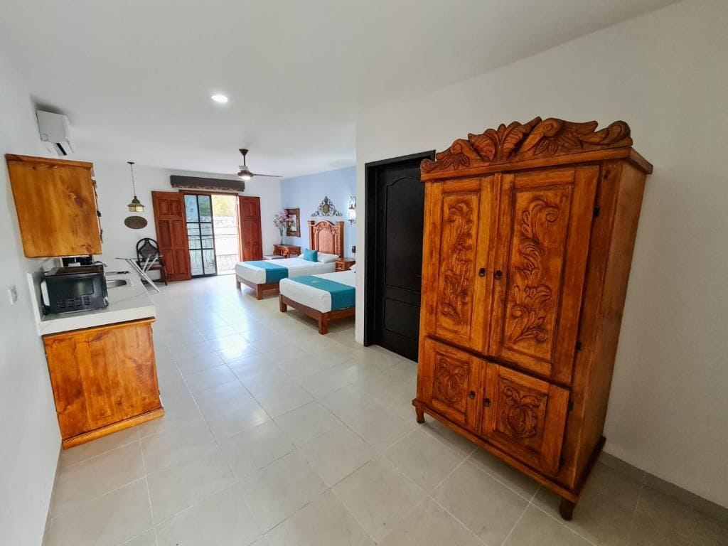 A spacious room with a bed, a wooden cabinet, and a kitchenette area.