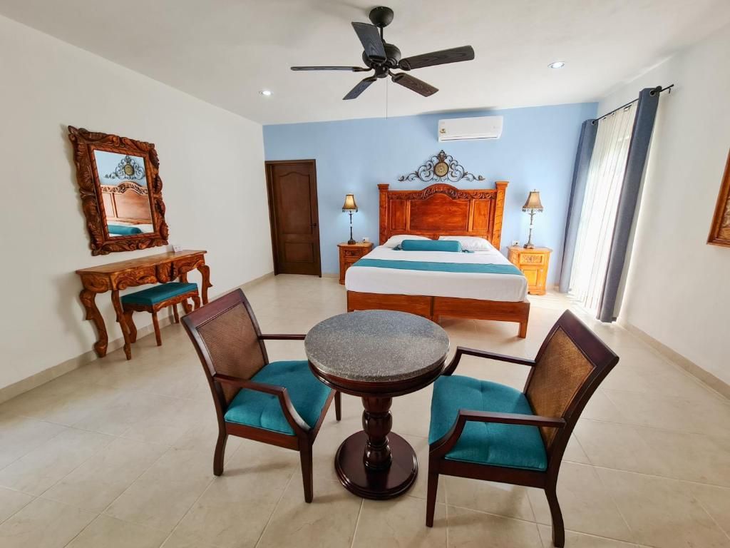 A hotel room with a bed, a round table with chairs, a ceiling fan, and a wooden dresser.