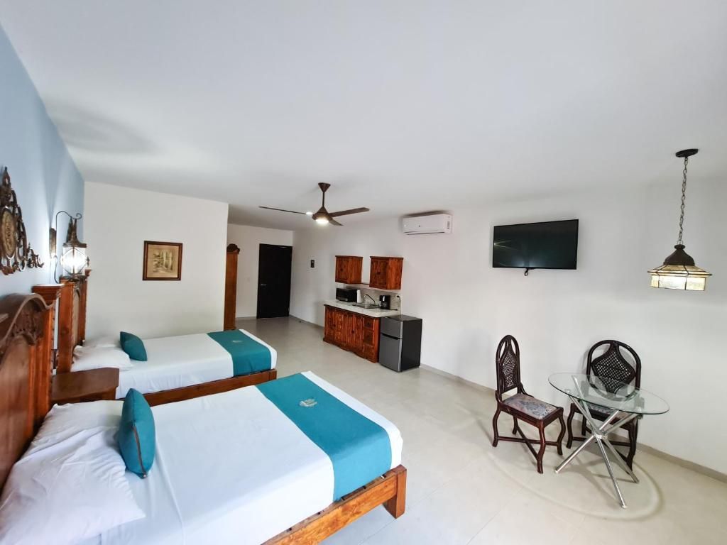 A hotel room with two beds, a kitchenette, a dining area with a glass table, and a TV mounted on the wall.