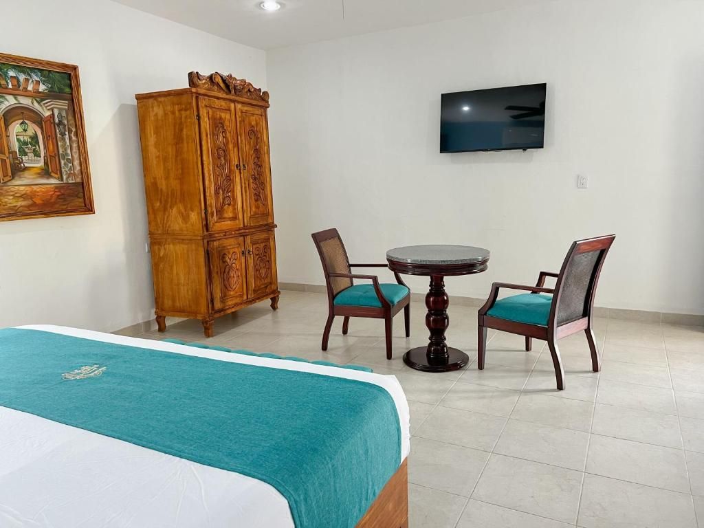 Une chambre d’hôtel comprenant un lit, une armoire en bois, une table ronde avec des chaises et un téléviseur à écran plat fixé au mur.