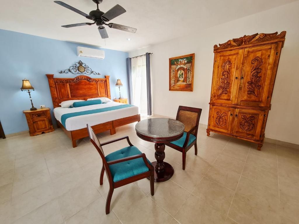 A hotel room with a bed, a round dining table with chairs, a ceiling fan, and a large wooden cabinet.