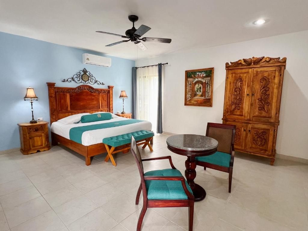 A hotel room with a bed, a round table with chairs, a ceiling fan, and a wooden cabinet.