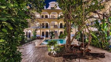 Un patio con piscina, rodeado de abundante vegetación y un edificio con varios balcones.