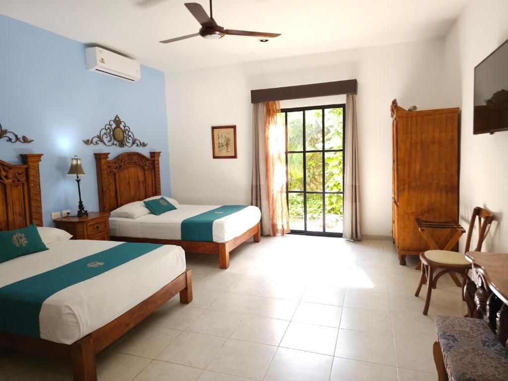 A hotel room with two wooden beds, a ceiling fan, a window with curtains, a wooden wardrobe, and a television on the wall.
