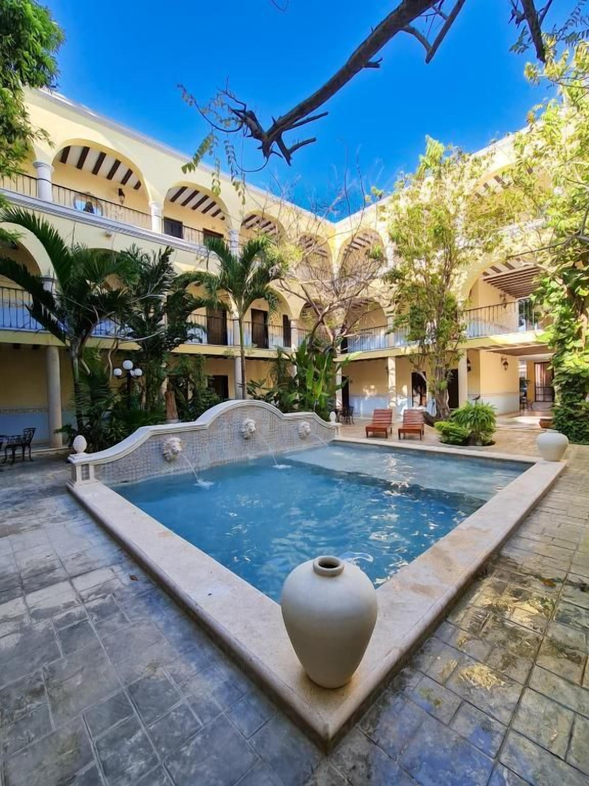 A courtyard with a swimming pool, palm trees, and a tiled floor.