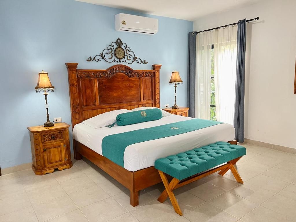 Ein Schlafzimmer mit einem hölzernen Bett, zwei Nachttischen mit Lampen, einer Bank und einem Fenster mit Vorhängen.