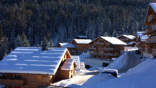A snow-covered lodge with multiple wooden cabins, a ski lift in the background, and a forested mountain.