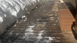 A wooden deck leading to a house with snow on the ground.
