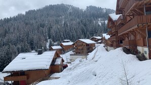 A snow-covered mountain village with wooden buildings, a ski slope, and a forested backdrop.