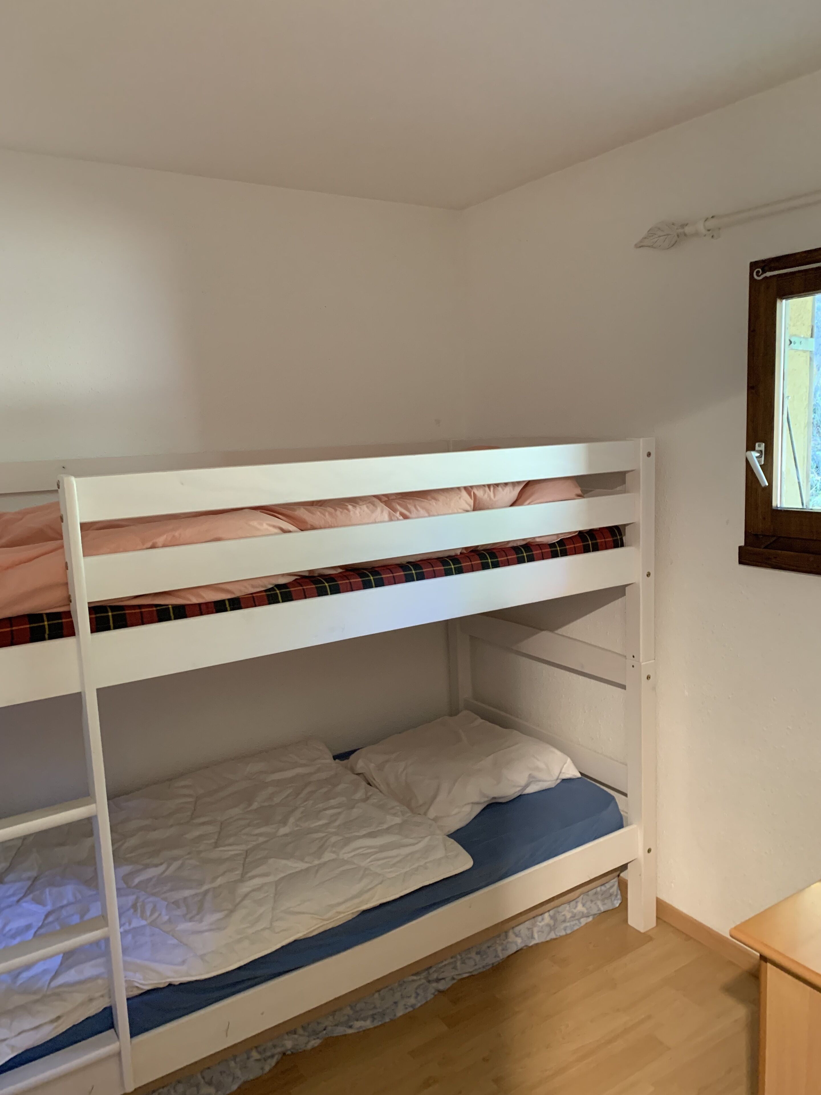 A bunk bed room with a window and a wooden nightstand.
