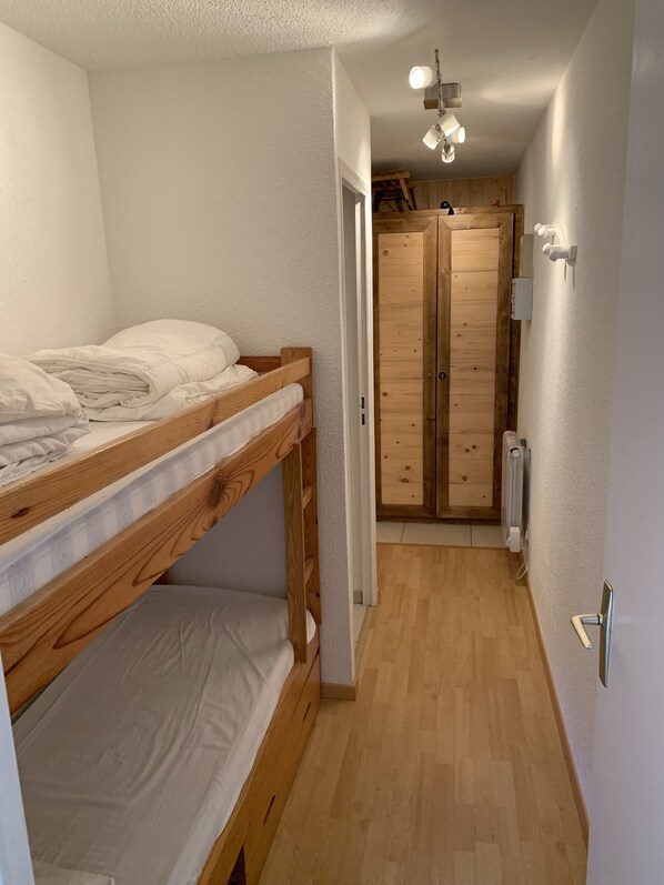 A bunk bed in a narrow hallway with a wooden wardrobe and a radiator.
