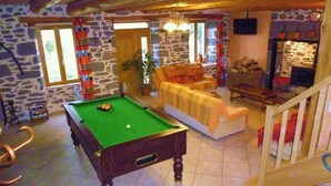 Una mesa de billar en una habitación con paredes de piedra, un sofá y una escalera.