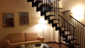 A living room with a wooden staircase, a sofa, a coffee table with teapots, and two framed pictures on the wall. - Castello Izzalini Todi Resort "Apt 4" (Izzalini)