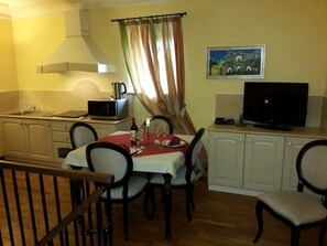 Un comedor con una mesa dispuesta para dos personas, un microondas, un televisor y un cuadro en la pared.