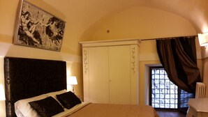 A bedroom with a large bed, a nightstand, a dresser, a painting on the wall, and a window with curtains. - Castello Izzalini Todi Resort "Apt 4" (Izzalini)